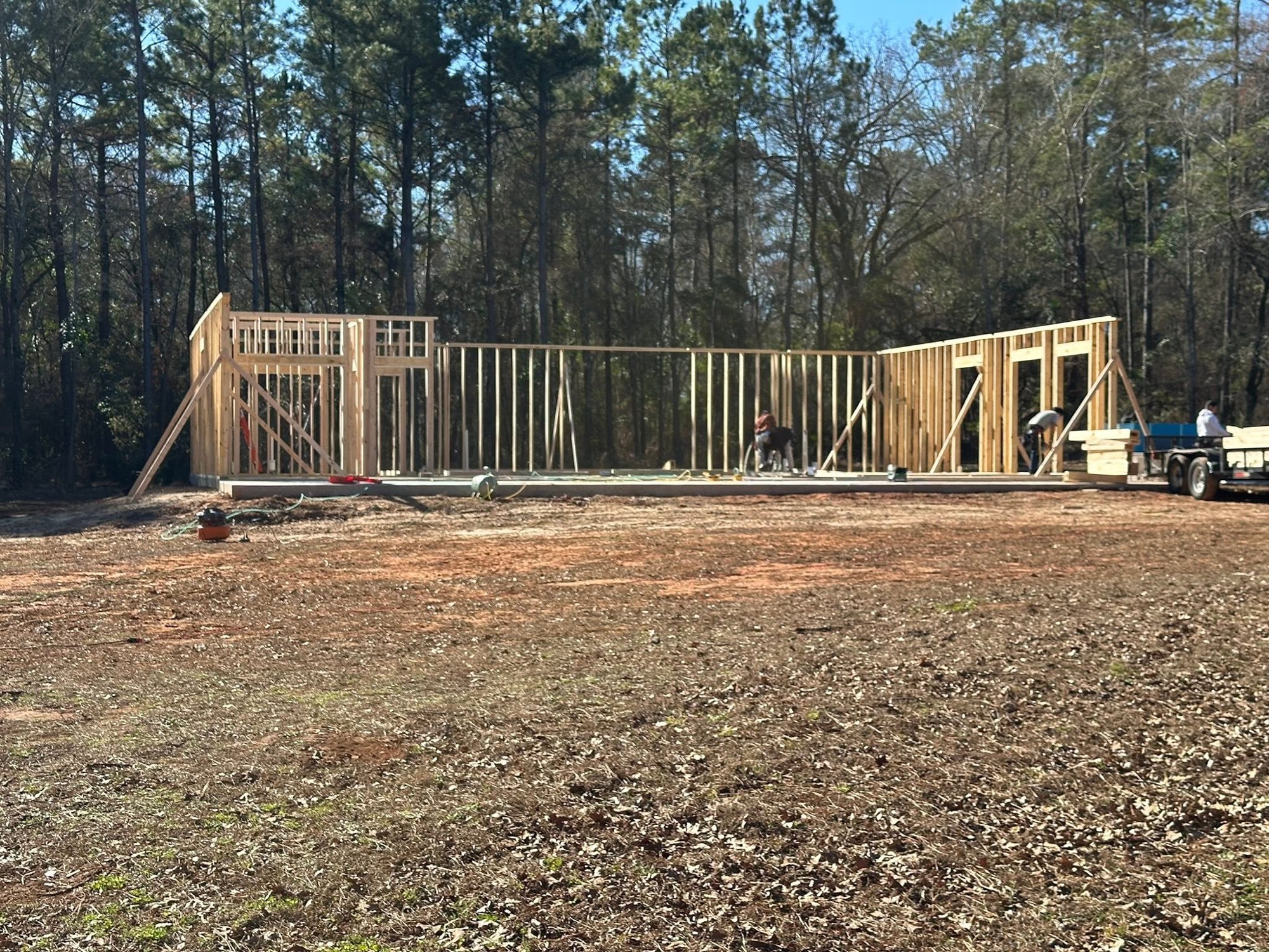 Wall framing going up on a cleared lot in the pines