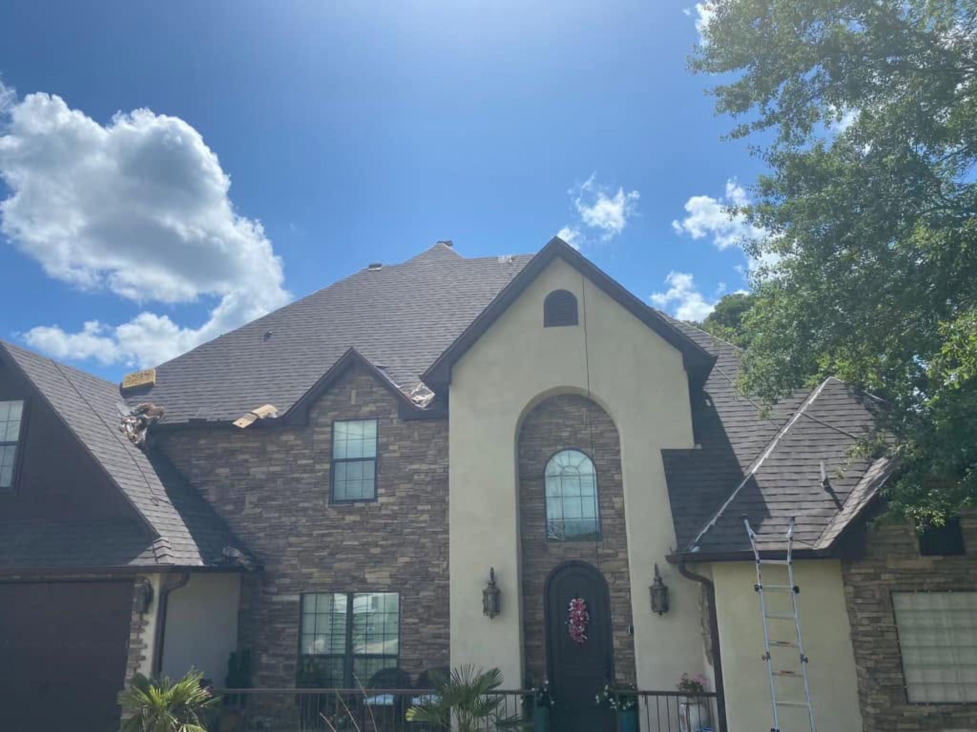 Ladder against the new roof of a stone and stucco home with an arched entry