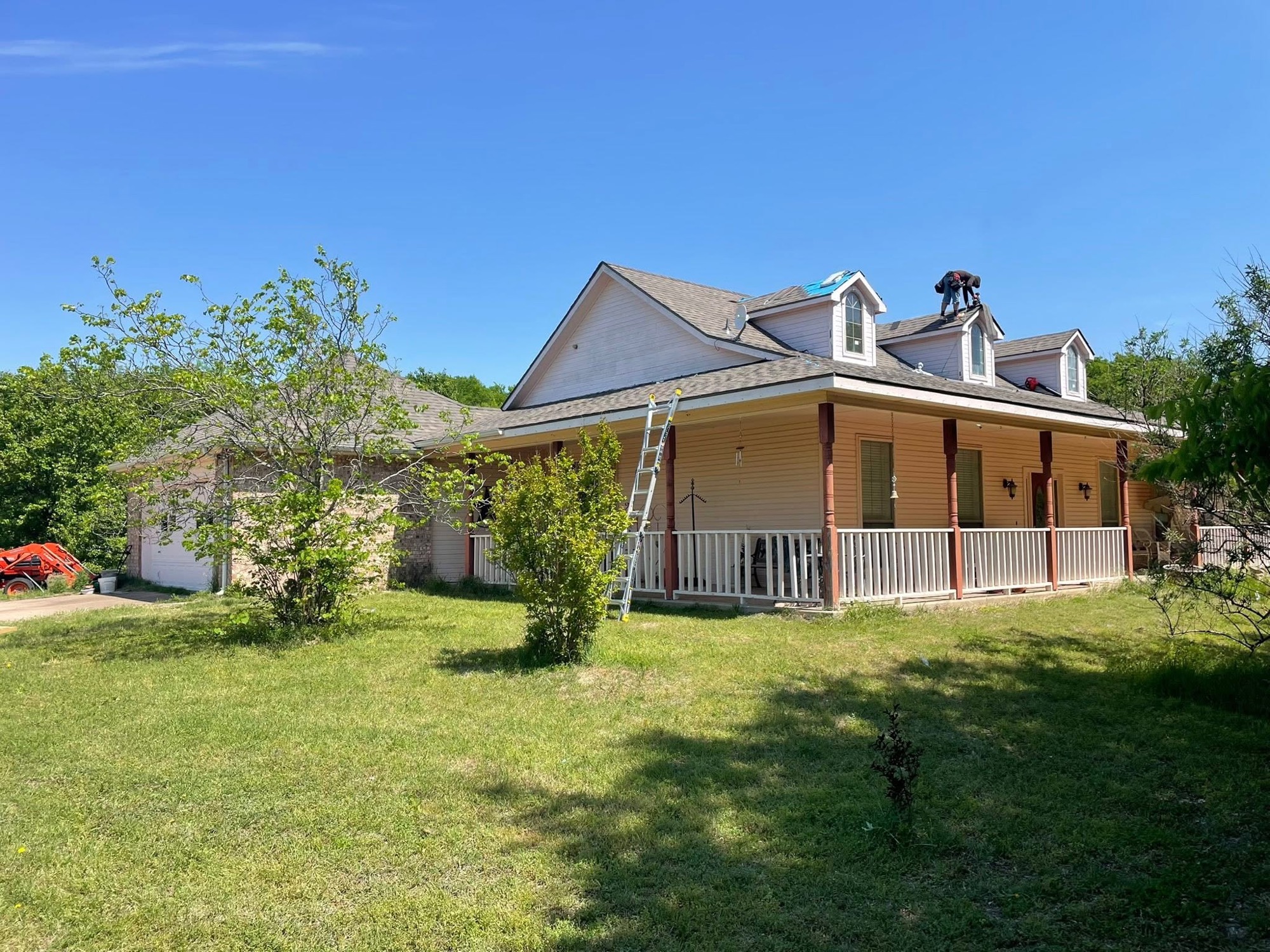 White farmhouse with a wraparound porch and a ladder up for a reroof